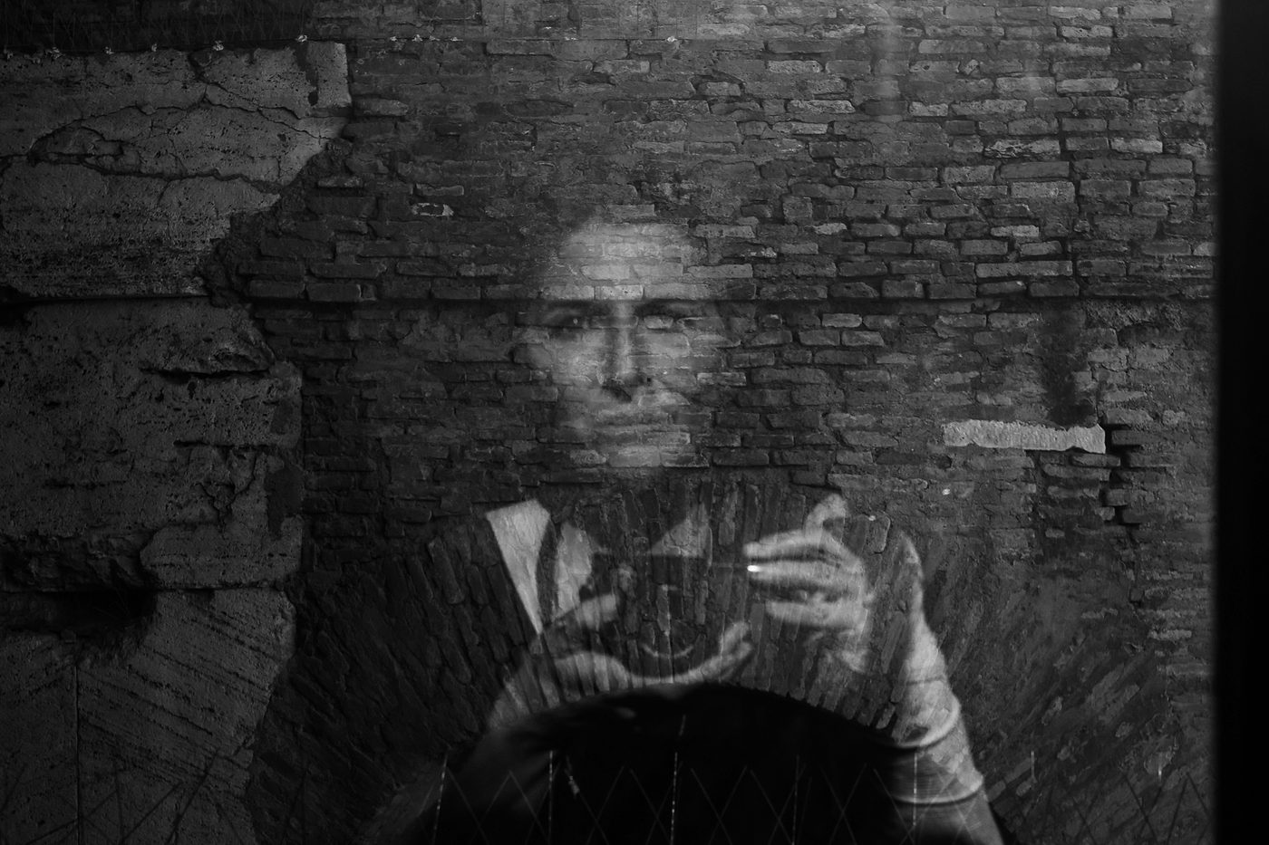 A self-portrait: the photographer's reflection, camera raised, dissolving into an old brick wall.